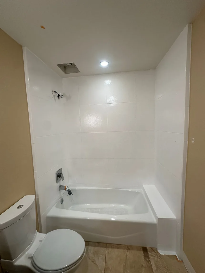 The same alcove refinished in white, walls and tub together, under the same ceiling light.