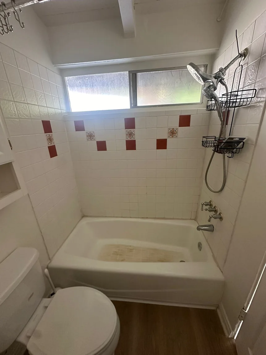 A white tiled bathroom with a band of red and patterned decorative tiles above the bathtub.