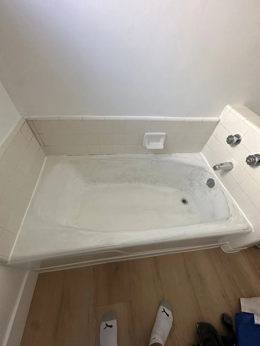 A bathtub with a dulled, scratched surface, surrounded by small white tile.