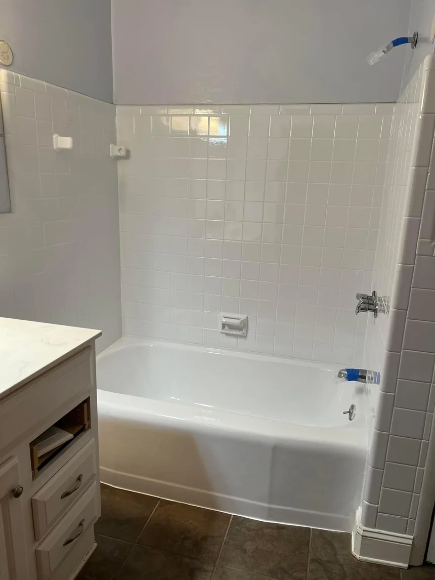 A refinished bathtub and white tile surround beside a vanity.