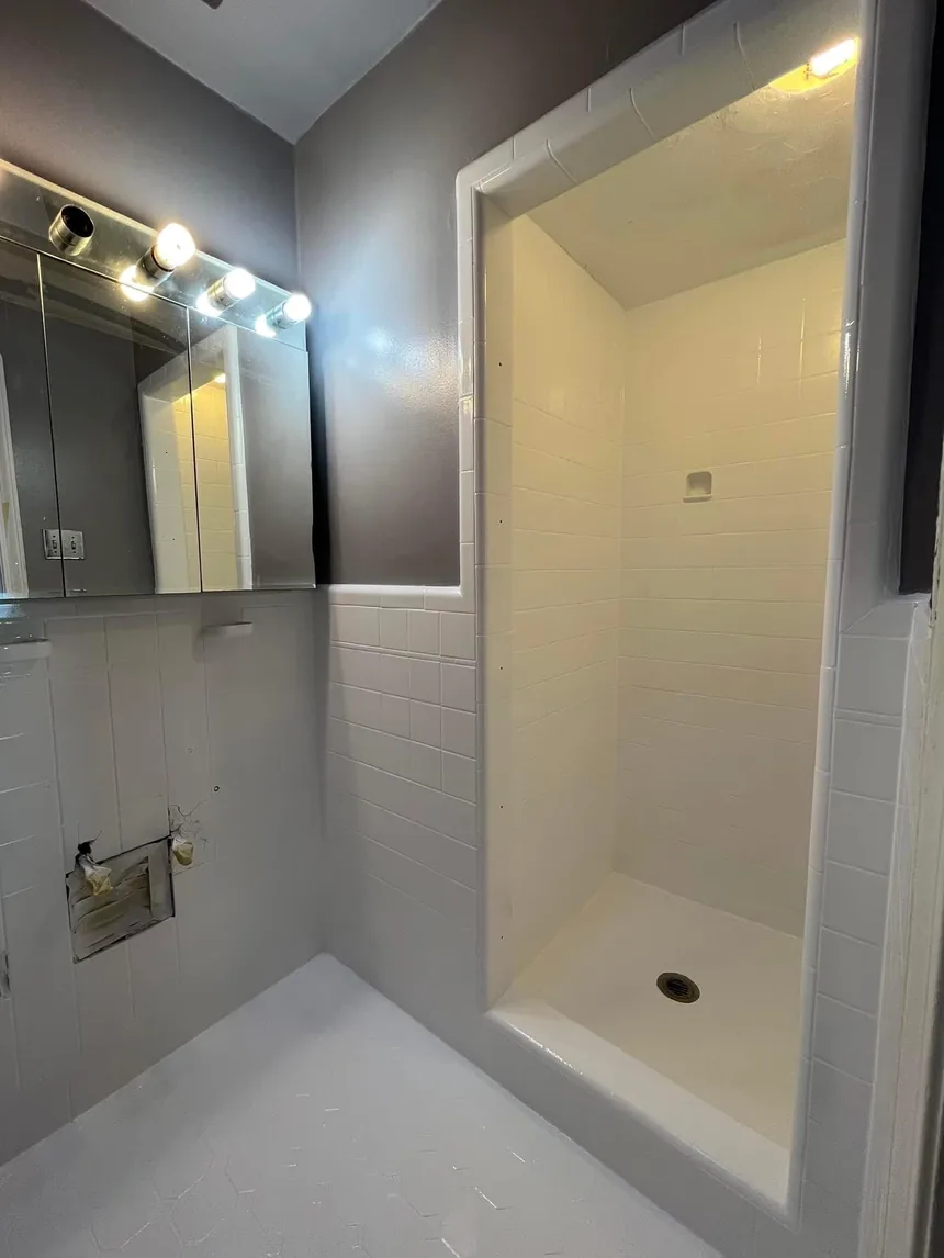 A 1950s bathroom refinished in white: walls, shower stall and hexagonal floor.