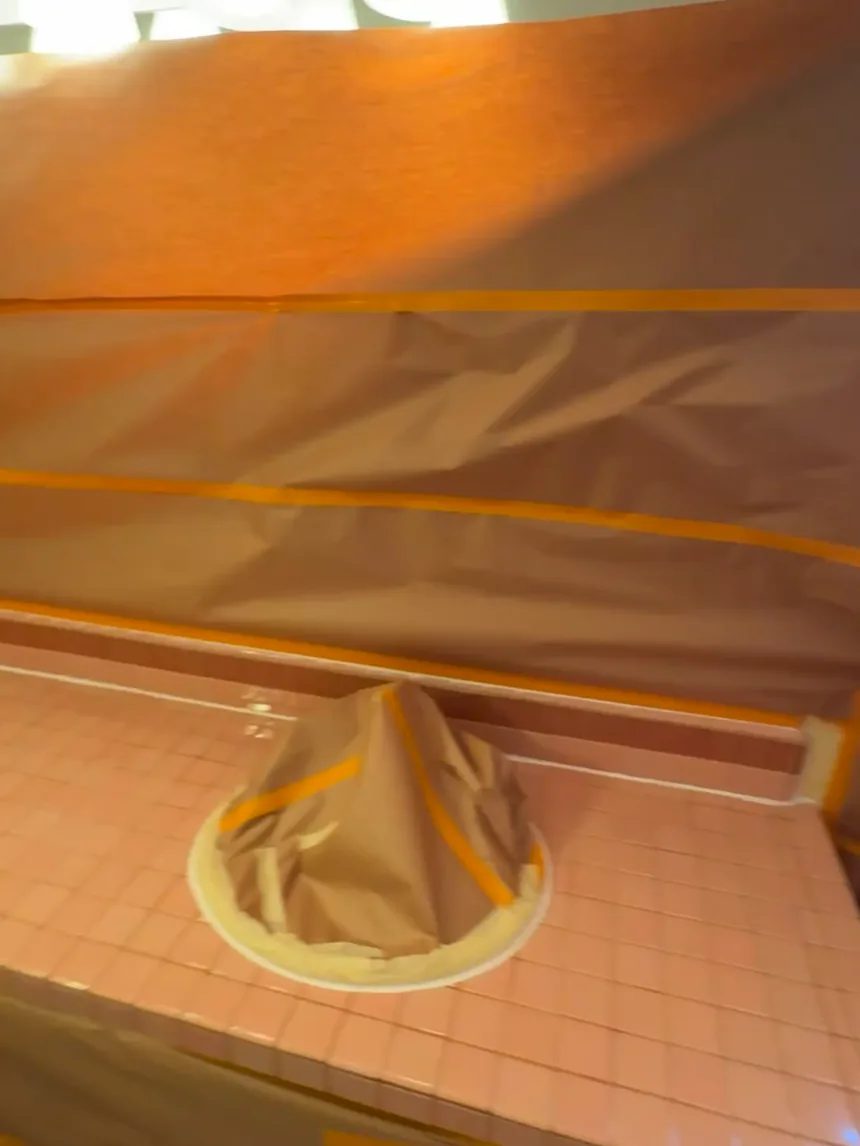 A tile countertop masked off for spraying: the sink covered with paper and tape, plastic sheeting taped to the wall behind.
